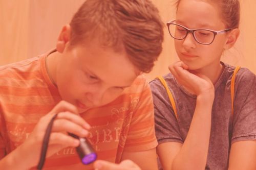 Chłopiec świecący latarką UV i przyglądająca mu się dziewczyna
