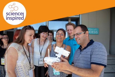 Grupa osób spogląda na przenośne urządzenie elektroniczne, w rogu zdjęcia logo Science Inspired