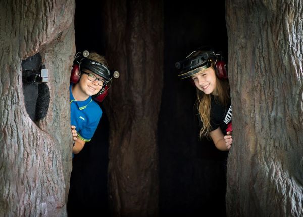 Dwoje dzieci stoi wewnątrz drzewa. Na głowach mają słuchawki pozwalające poznać zjawisko echolokacji.