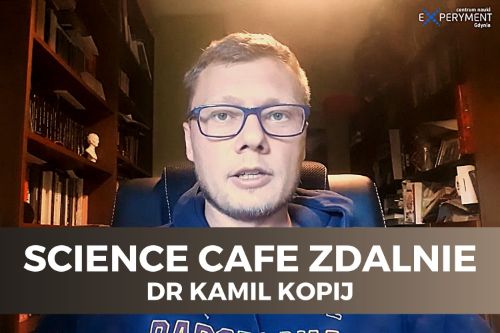 Science cafe zdalnie. Dr Kamil Kopij siedzi na skórzanym krześle. Po obu bokach stoją regały z książkami. Ma okulary w niebieskich oprawkach i niebieską bluzę.