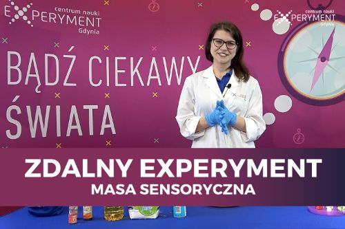 Zdalny experyment, masa sensoryczna. Edukatorka stoi przed blatem z kolorowymi przedmiotami potrzebnymi do eksperymentów.