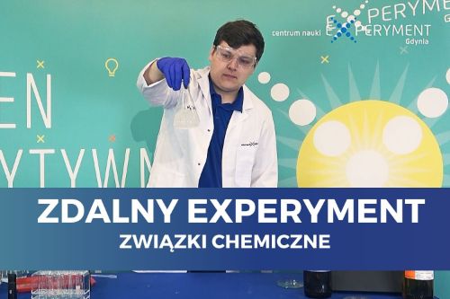 Zdalny experyment, związki chemiczne. Edukator w fartuchu i goglach ochronnych trzyma w ręku kolbę z przezroczystą cieczą.