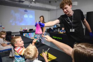 uro2 edukator podaje dzieciom zlewkę z fioletowym płynem