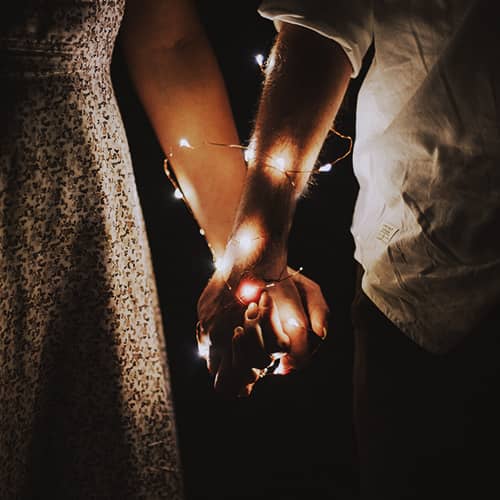 Para trzymająca się za ręce, splecione i obwiązane lampkami.