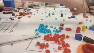 IMG_20190413_184840 Zdjęcie zrobione zostało podczas wydarzenia Space Game Jam, podczas którego uczestnicy w grupach tworzą grę planszową według wcześniej wylosowanej tematyki. Na zdjeciu przedstawiono prototyp planszy gry, na której umieszczone jest kilka różnego rodzaju pionków i znaczników. Z lewej strony fotografii przygotowywana jest rozpiska z zasadami czy też punktami jakie można otrzymać w grze planszowej.