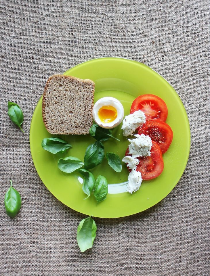 Talerz z lekkim śniadaniem z pomidorami, jajkiem, ziołami i ciemnym pieczywem.