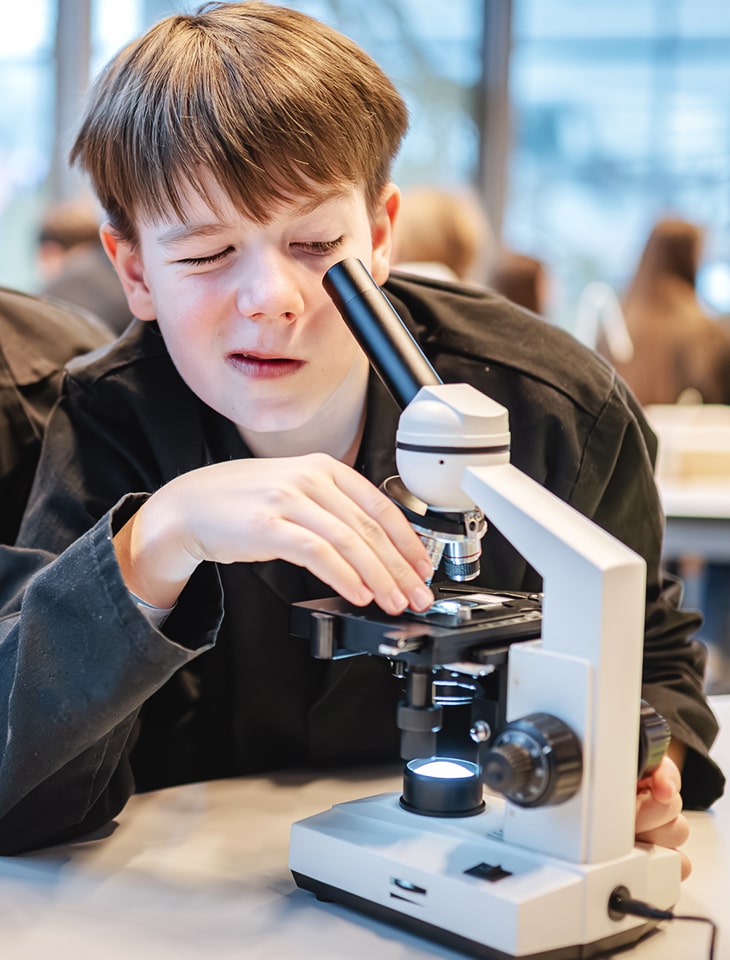 Zdjęcie przedstawia chłopca patrzącego przez mikroskop.