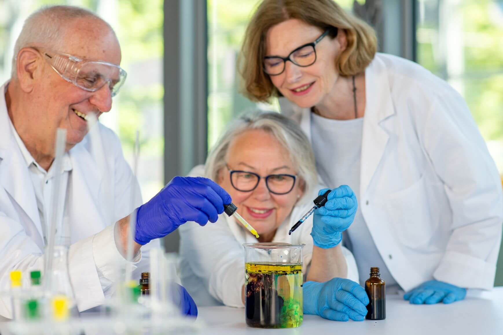 Trójka seniorów nad szkłem laboratoryjnym z pipetami i w gumowych rękawiczkach