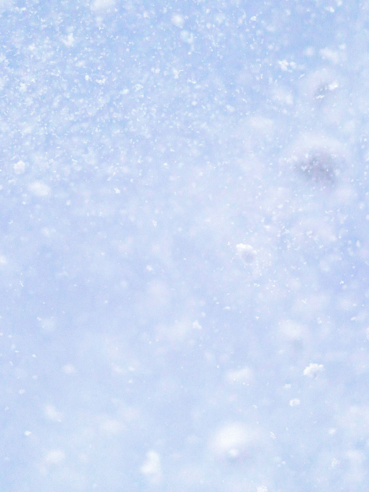 Rozmyte, jasnoniebieskie tło z wirującymi w powietrzu drobnymi płatkami śniegu, przypominające zamieć śnieżną.