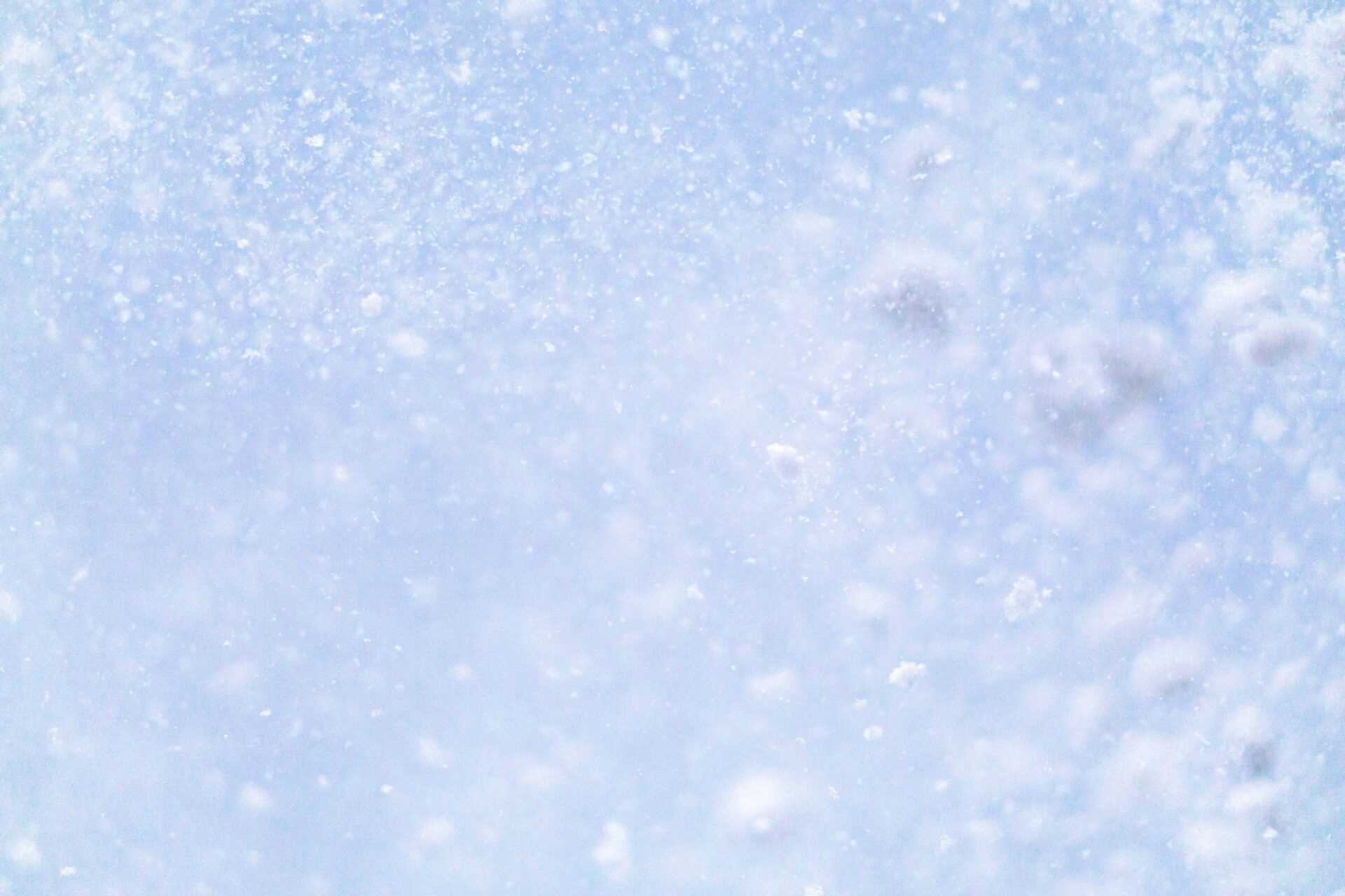 Rozmyte, jasnoniebieskie tło z wirującymi w powietrzu drobnymi płatkami śniegu, przypominające zamieć śnieżną.